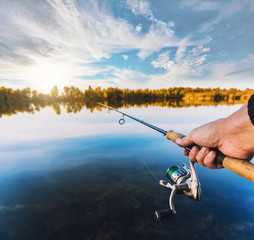 hand with spinning and reel on the summer lake