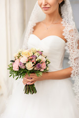 Wedding. Beautiful bride in luxury wedding dress with stylish veil holding colorful wedding bouquet