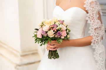 Wedding. Beautiful bride in luxury wedding dress with stylish veil holding colorful wedding bouquet