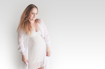 Young pregnant woman in pajamas, studio portrait on gray. Copy space