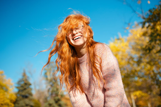 Portraits of a charming red-haired girl with a cute face. Girl posing in autumn park in a sweater and a coral-colored skirt. The girl has a wonderful mood