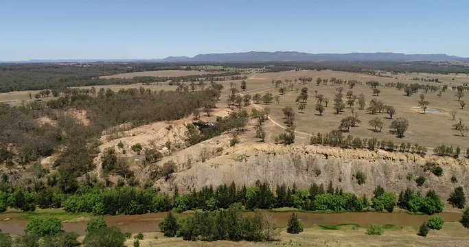 Narrow creek of Hunter River in arid drought climate across outback with lonely gumtrees on remote farm in Hunter Valley.