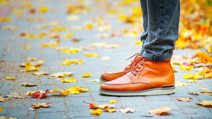 legs of a man in brown boots on the sidewalk strewn with fallen leaves. The concept of turnover of...