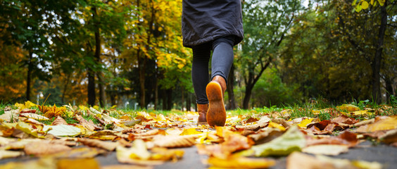 A woman in black jacket walking in a park along the sidewalk strewn with fallen leaves. The concept...