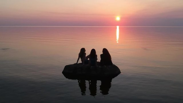 Wide shot of three woman a rock lava landscape by the sea at dusk in slow motion