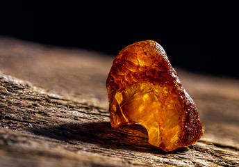 Natural amber. A piece of yellow transparent natural amber on large piece of dark stoned wood.