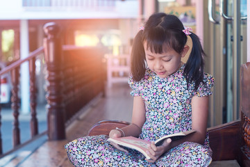 Cute asian child girl reading a book at home