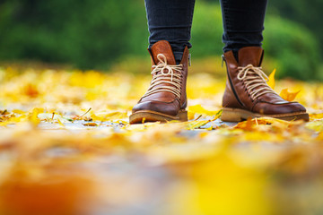 legs of a woman in black pants and brown boots in autumn park on sidewalk strewn with fallen...
