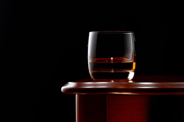 A glass of whiskey on a wooden table in a low key