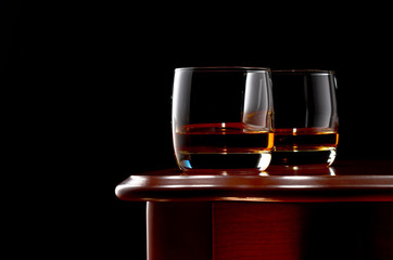 Two glasses of whiskey on a wooden table in a low key.