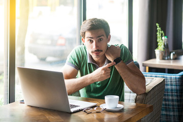 You have no more time! Young serious bossy businessman in green t-shirt sitting, looking at camera...