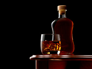 A glass with a double shot of whiskey and ice on wooden table. In the background, a full, closed...