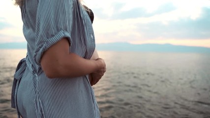Close-up of pregnant woman's body, healthy pregnancy and unborn baby yet. Relaxed woman walking along the beach in sunset. Future mother hugging her belly lovely and feeling silence. Family concept
