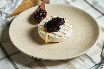 Close up view grilled Camembert cheese head on plate and on cutting board with jam. light texture background. Top view with copy space. Tasty food for breakfast.