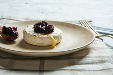 Close up view grilled Camembert cheese head on plate and on cutting board with jam. light texture background. Top view with copy space. Tasty food for breakfast.