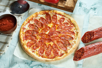 Homemade oven-baked pepperoni pizza with tomatoes, cheese, salami, red sauce. Composition with crispy pizza, tomatoes on a light background. Copy space. Top view