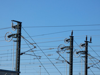 Catenaria y cables en la vía del tren, Cables electricos que hacen llegar la electricidad al tren, Cielo azul y tecnología en las vías del tren.
