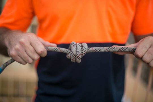 Closeup pic of male rope access industrial worker, tying a knot into static twin ropes before working and abseiling off from high rise building in circular quay, Sydney city CBD, Australia 