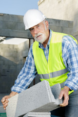 senior man holding a bloc of cement outdoors