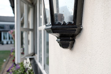 Shallow focus view of a metal security lantern seen attached to a separate building to the main house, seen with the window ajar.