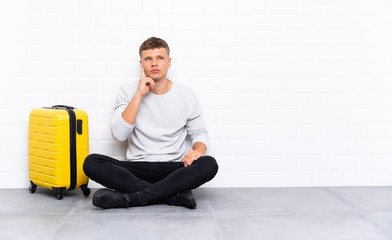 Young handsome man sitting on the floor with a suitcase thinking an idea