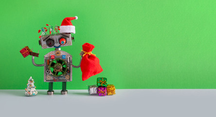 Santa Claus steampunk robotic toy with gifts bag on green background. Festive Christmas New year greeting card mockup with funny robot dressed red Santa hat. empty space backdrop for text