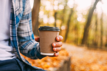 Paper cup of coffee in man hand in the autumn park