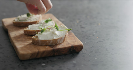 man hand decorating ciabatta with cream cheese with pea sprouts