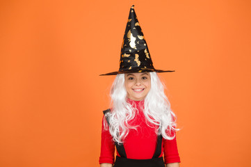 in holiday mood. magic fantasy. smiling girl halloween party. mystery witch. small child witch hat. trick or treat. supernatural charmer gray hair. kid enchantress orange background. happy halloween