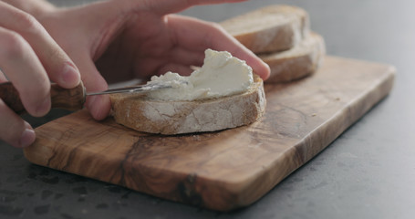 man hand spreading ricotta on slice of ciabatta