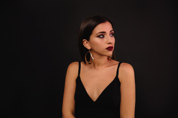 Studio shot of attractive pretty woman wearing black dress with bare shoulders posing over black background