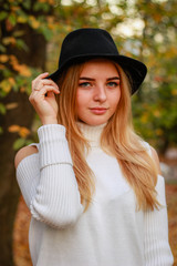 Autumn girl portraits. Model in a white sweater. Black hat. Yellow leaves. Atmospheric photos.