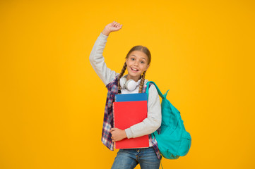 She likes school. Happy girl with raised hand yellow background. Small girl ready back to school. Little girl celebrate September 1. Cute girl smile with school bag and books. Startup