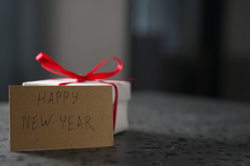 White gift box with red ribbon and happy new year paper card on terrazzo surface