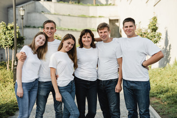 Happy family in white T-shirt and jeans emracing and having fun. Parents with their adult children walking in the park. Family time concept