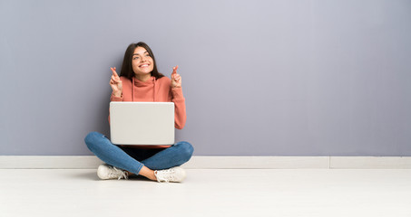 Young student girl with a laptop on the floor with fingers crossing