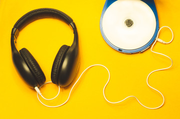Headphones with a white cable on a yellow background. compact disc player with white cd and earphones