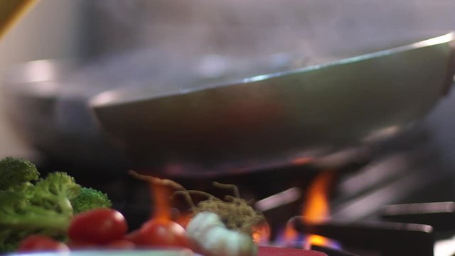 Chef preparing spaghetti in frying pan on gas kitchener in the kitchen in slow motion. Fresh vegetables in the foreground.
