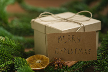 Eco brown paper gift box surrounded by christmas decorations and spruce branches with merry...