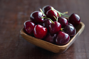 Ripe fresh cherries in a wooden bowl. Food background. Red juicy cherry berry on brown wooden background. Cherries in a dish closeup.