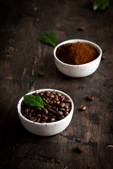 coffee beans and ground coffee in bowls with coffee tree leaf on a dark background.