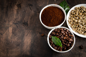 coffee beans and ground coffee in bowls with coffee tree leaf on a dark background. copy space for your text