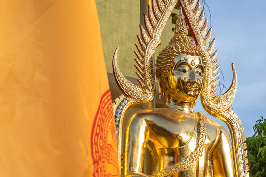 The golden Buddha face and the Buddhist yellow flag in outdoor of the temple in Thailand with the blue sky copy space