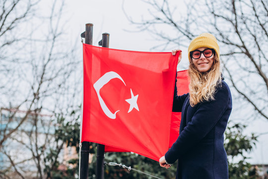 A girl in a yellow hat is photographed in a park with the flag of Turkey in the winter. A tourist walks through the autumn park in Istanbul.