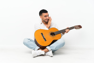 Young man sitting on the floor with guitar whispering something