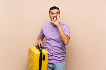 Man holding a suitcase over isolated background shouting with mouth wide open
