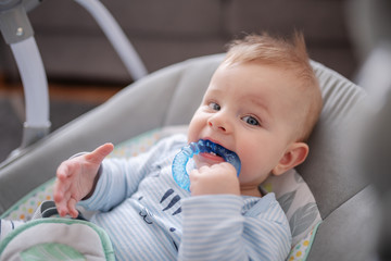 Head shot of adorable baby boy lying in rocker chair and biting teether.