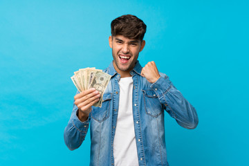 Young handsome man over isolated blue background taking a lot of money