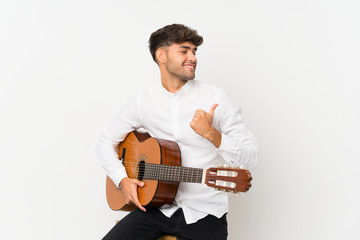 Young handsome man with guitar over isolated white background pointing to the side to present a product