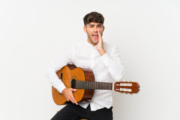 Young handsome man with guitar over isolated white background shouting with mouth wide open